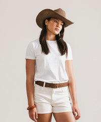 Person wearing a white t-shirt, white shorts, and a brown cowboy hat on a plain background