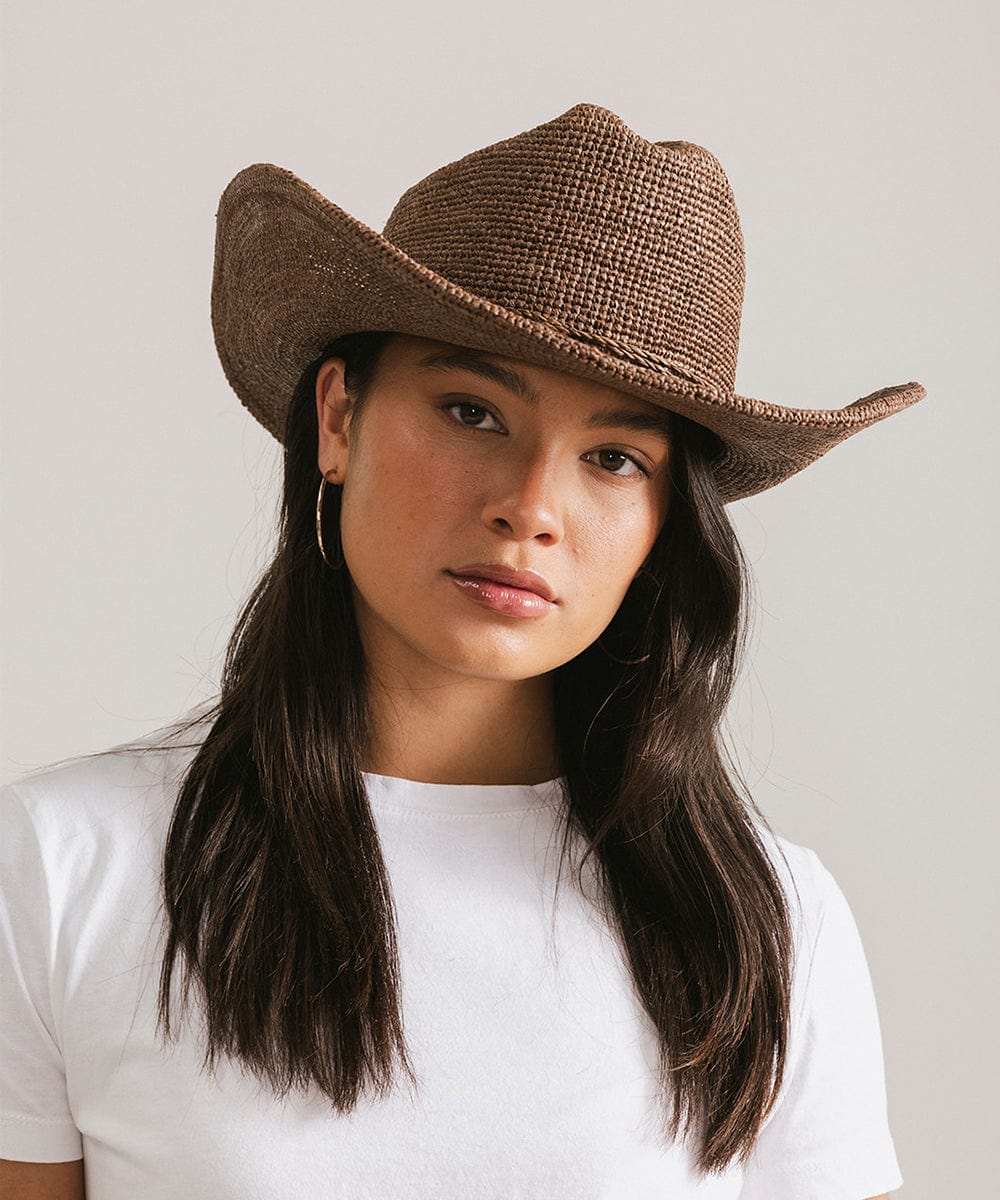 Woman wearing a brown cowboy hat against a plain background