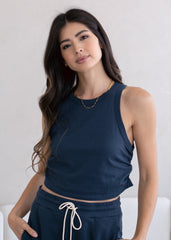 Woman wearing a navy blue sleeveless top and dark pants against a white background