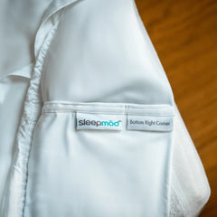 White fitted sheet with 'sleepmod' label on a wooden surface