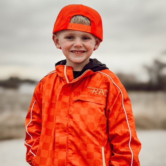 Child wearing an orange checkered jacket and cap outdoors