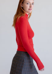 Woman wearing a red long-sleeve top and plaid skirt on a light gray background