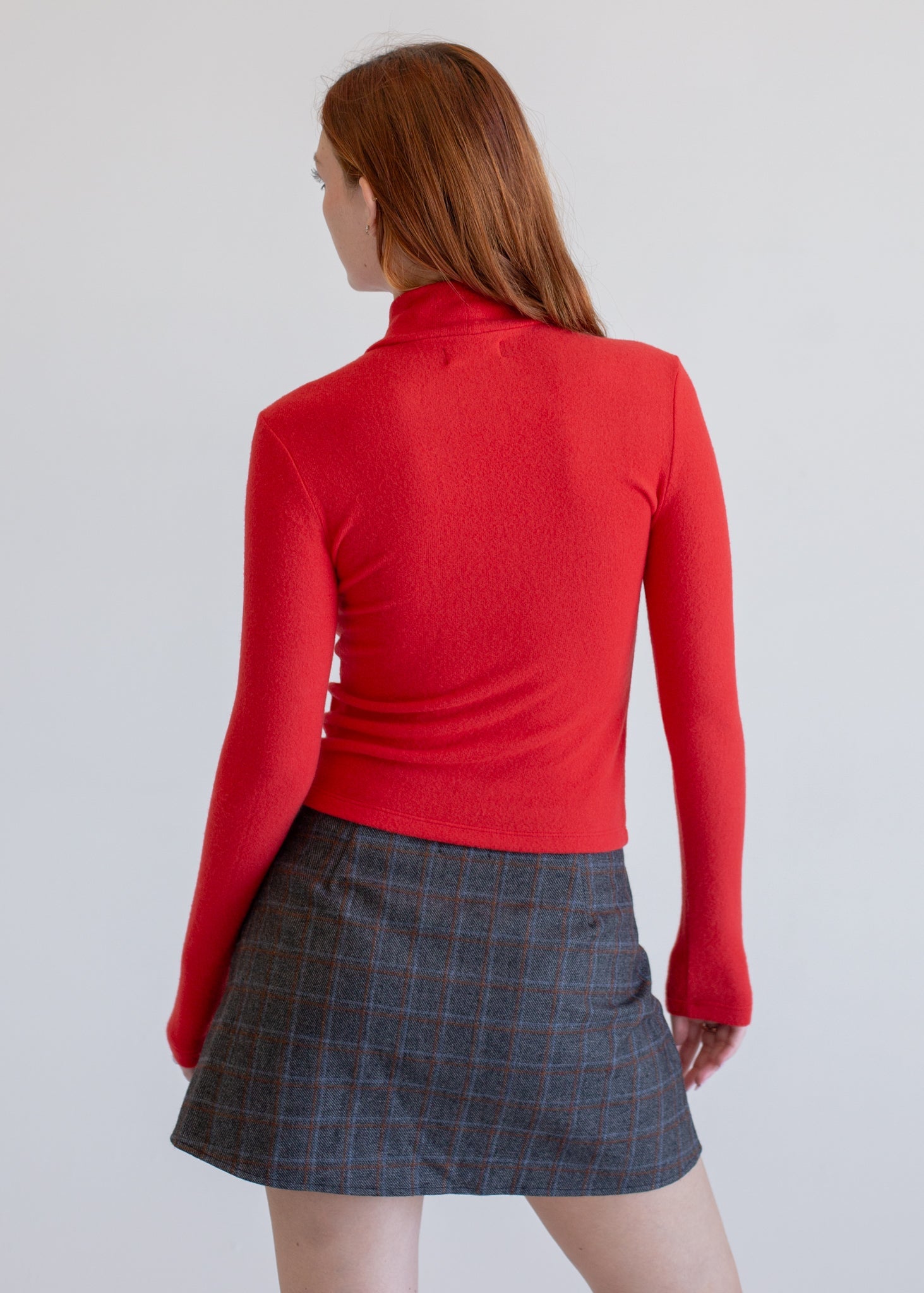 Person wearing a red sweater and gray checkered skirt on a plain background