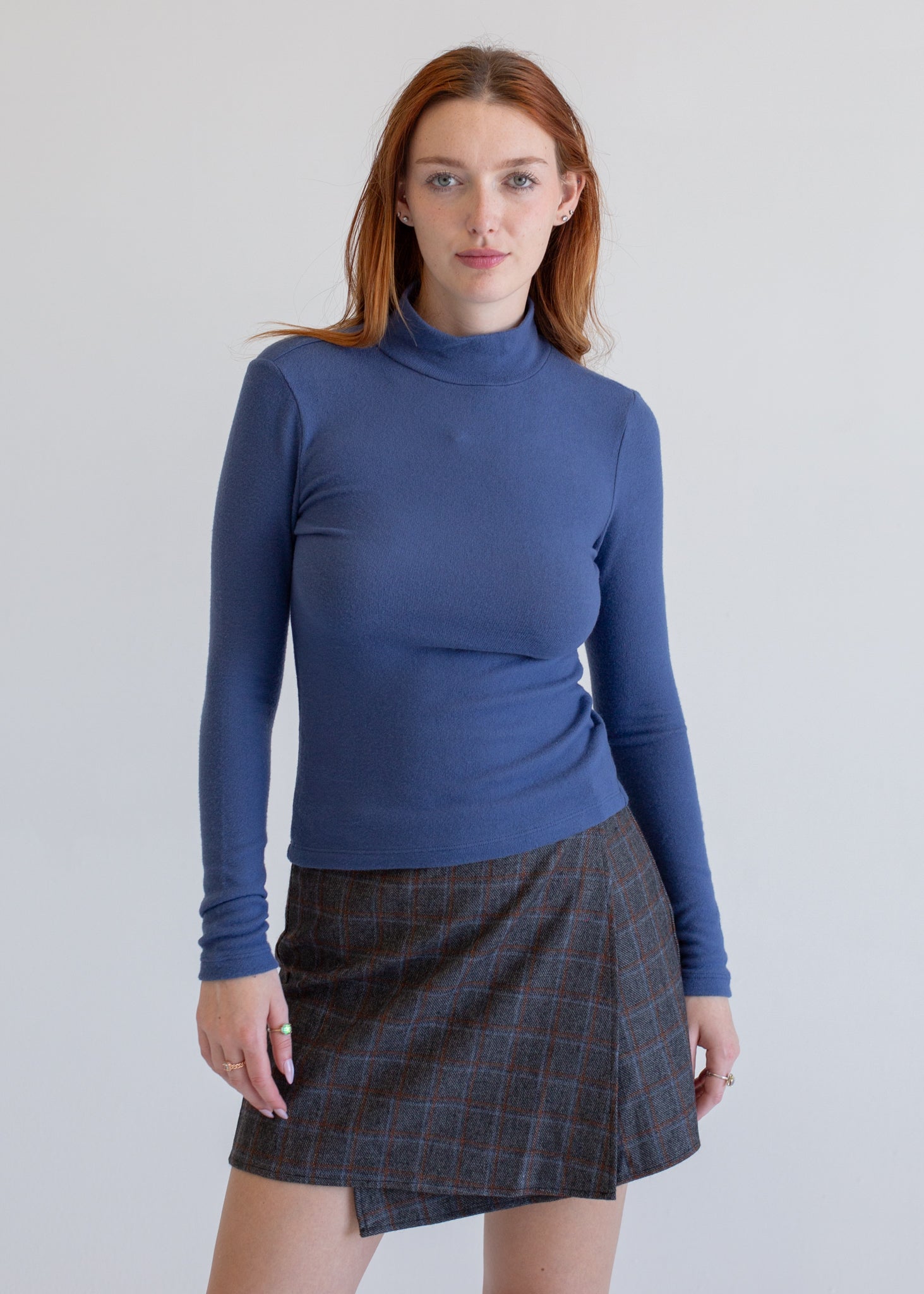 Woman wearing a blue turtleneck sweater and plaid skirt on a plain background