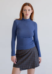 Woman wearing a blue turtleneck sweater and plaid skirt on a plain background
