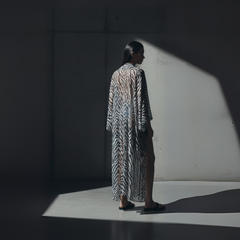 Person wearing a patterned dress standing in a spotlight against a dark background