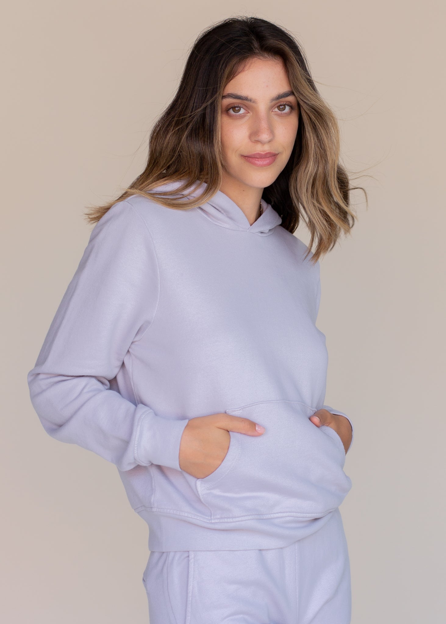 Woman wearing a light purple hoodie and pants against a beige background