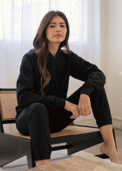 Woman in a black outfit sitting on a chair with a neutral background