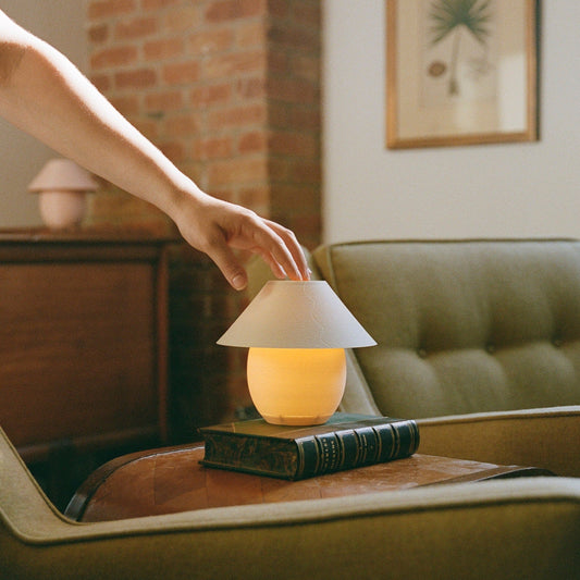 Hand adjusting a small lamp on a book in a cozy living room.