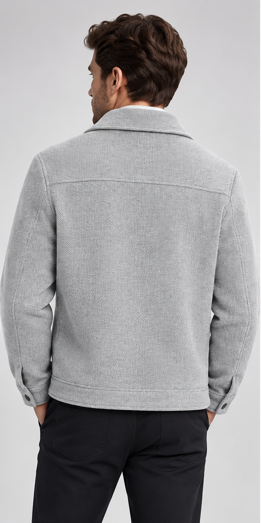 A man viewed from the back wearing a light gray textured jacket and dark trousers, photographed against a plain light gray studio background.