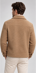 A man shown from the back wearing a tan textured jacket and light beige trousers against a light gray studio background.