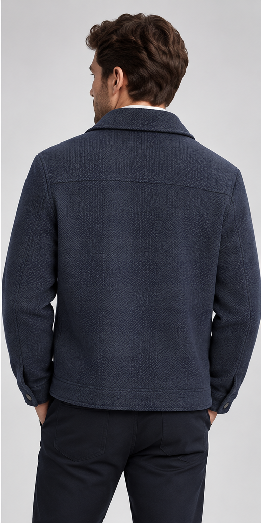 A man viewed from the back wearing a dark navy textured jacket and dark trousers against a light gray studio background.