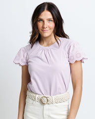 Woman wearing a light purple blouse with lace sleeves on a plain background