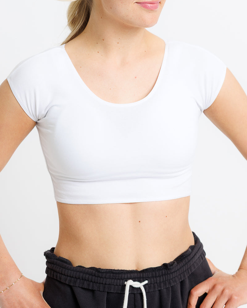 Person wearing a white crop top and black pants on a plain background