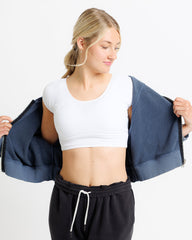 Woman wearing a white crop top and black pants, holding a navy jacket against a white background