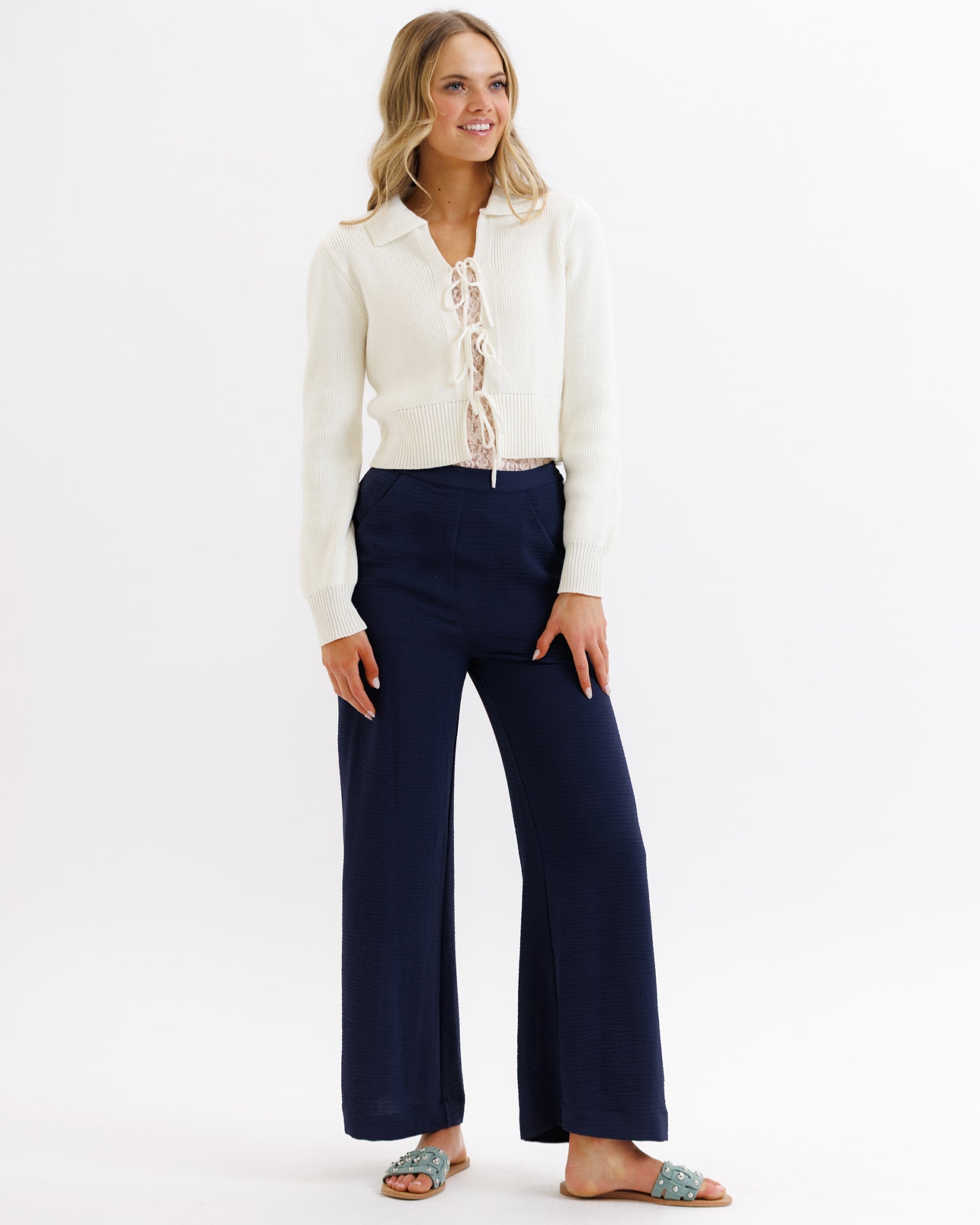 Woman wearing a white blouse and navy pants on a white background