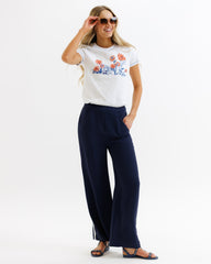 Woman wearing a white t-shirt with floral design and navy pants on a white background