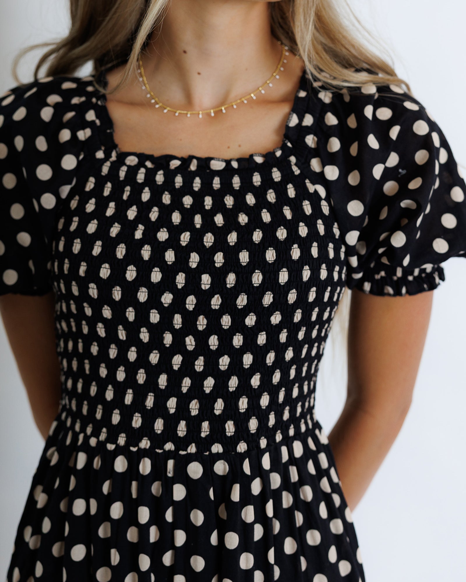 Black dress with white polka dots worn by a person on a plain background