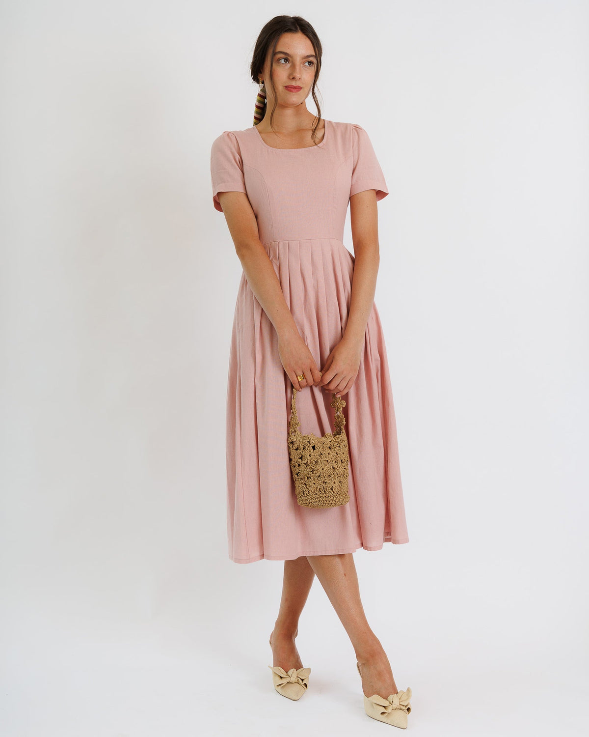 Woman wearing a pink dress holding a woven bag on a white background