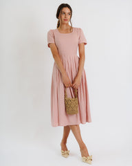 Woman wearing a pink dress holding a woven bag on a white background