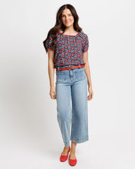 Woman wearing a floral blouse, jeans, and red shoes on a white background