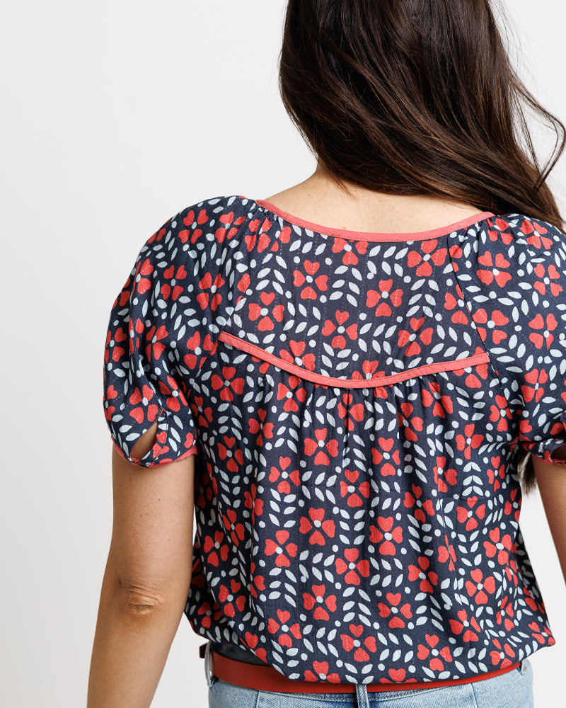 Woman wearing a floral patterned top with red and white flowers on a plain background