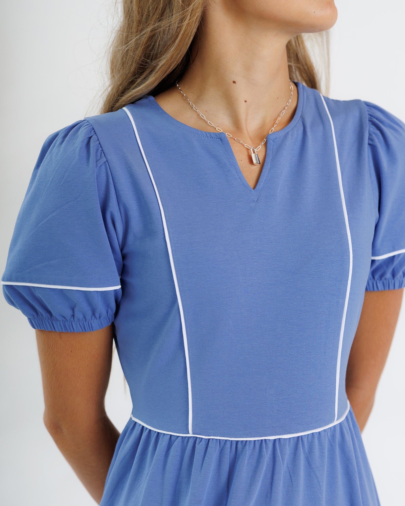 Blue dress with white trim worn by a person on a plain background
