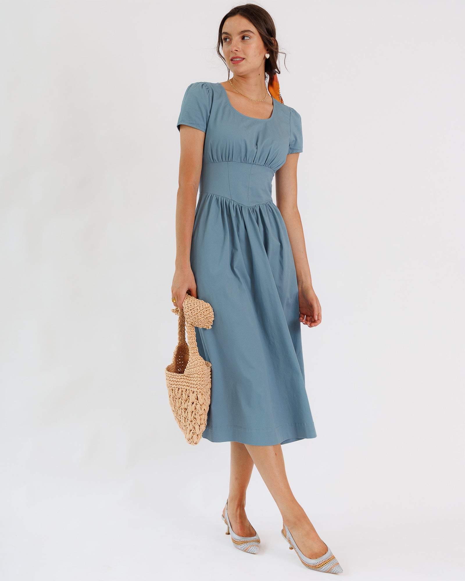 Woman wearing a blue dress holding a woven bag on a white background