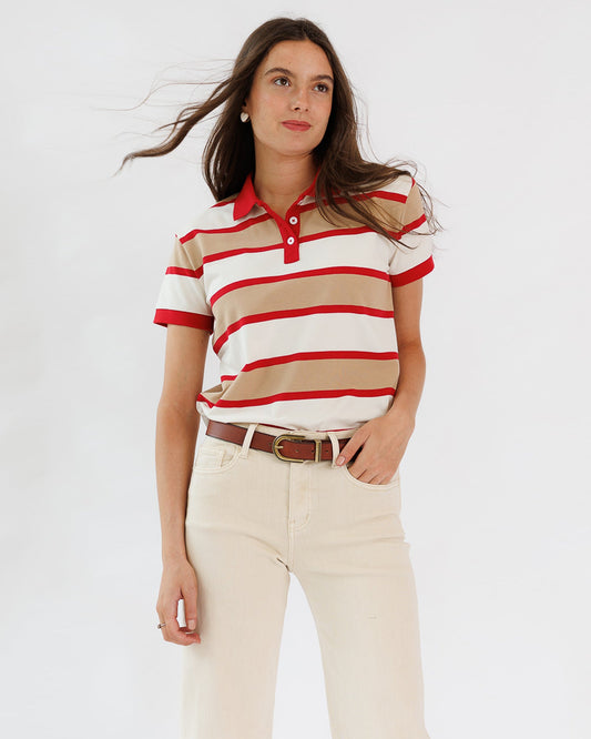Woman wearing a red and beige striped polo shirt with white pants on a light gray background