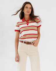 Woman wearing a red and beige striped polo shirt with white pants on a light gray background