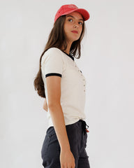 Woman wearing a white t-shirt with black trim and a red cap on a plain background