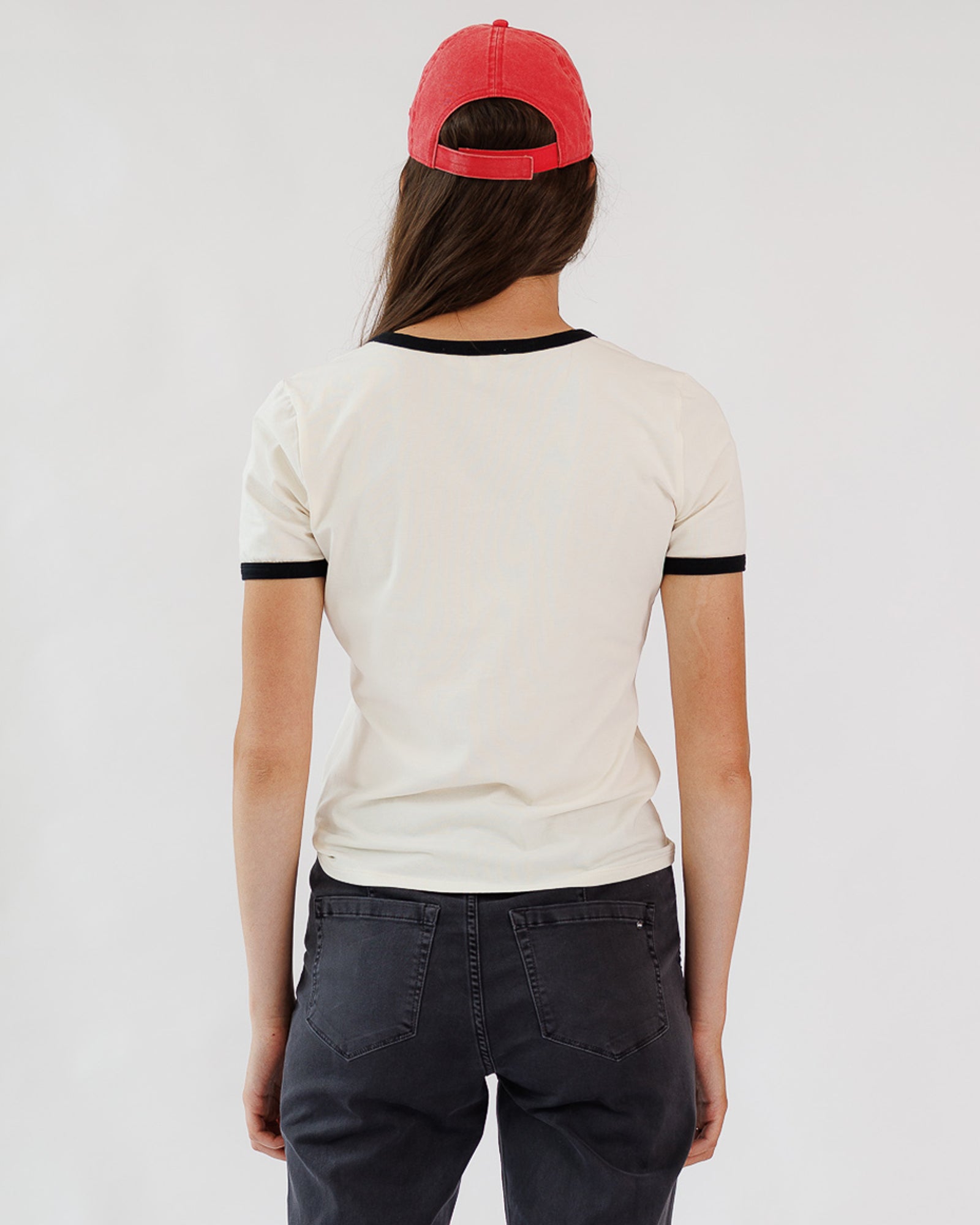 Person wearing a white t-shirt with black trim and a red cap on a plain background