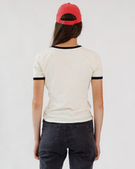 Person wearing a white t-shirt with black trim and a red cap on a plain background