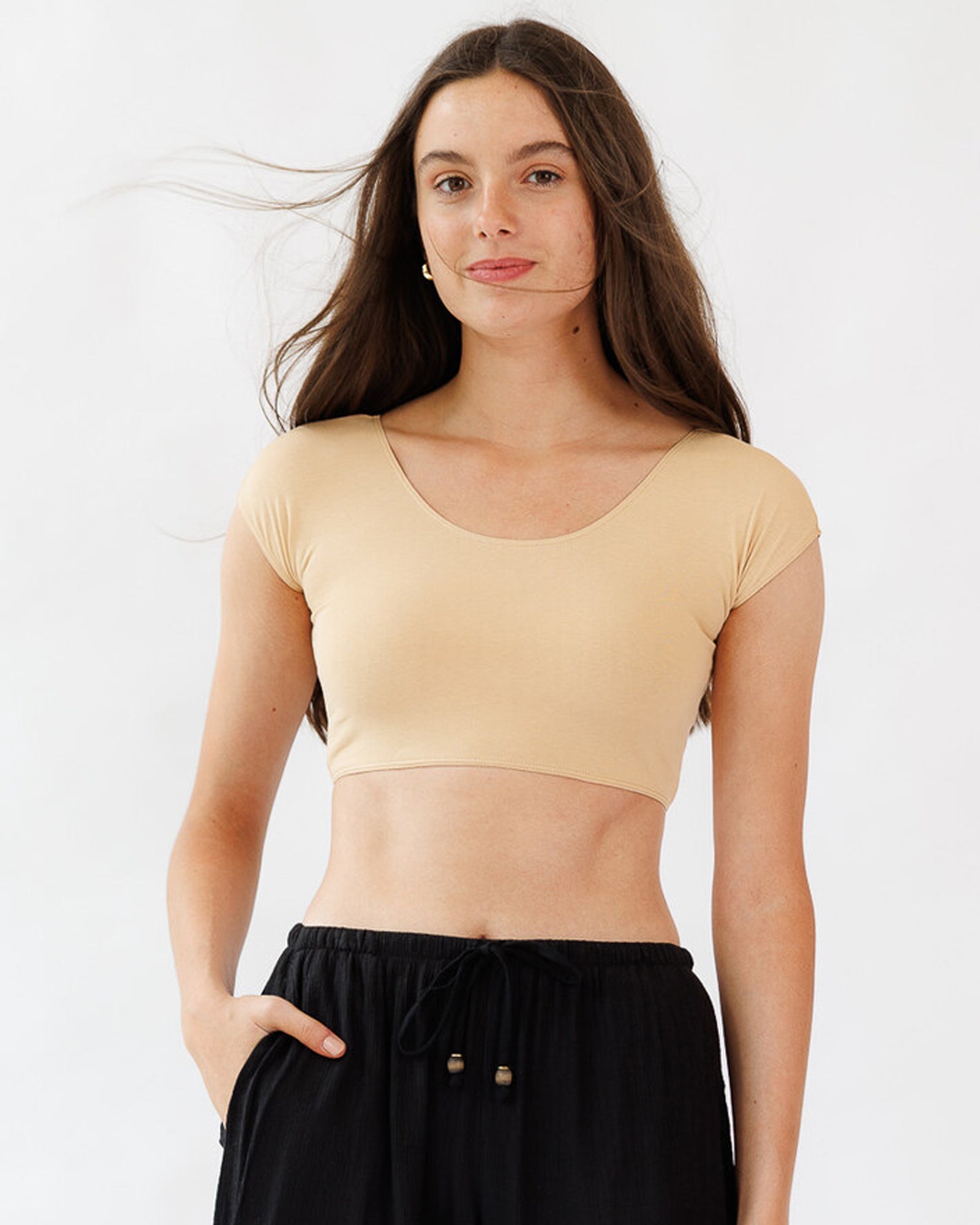 Woman wearing a beige crop top and black pants against a white background