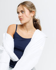 Woman wearing a navy tank top and white cardigan against a plain background