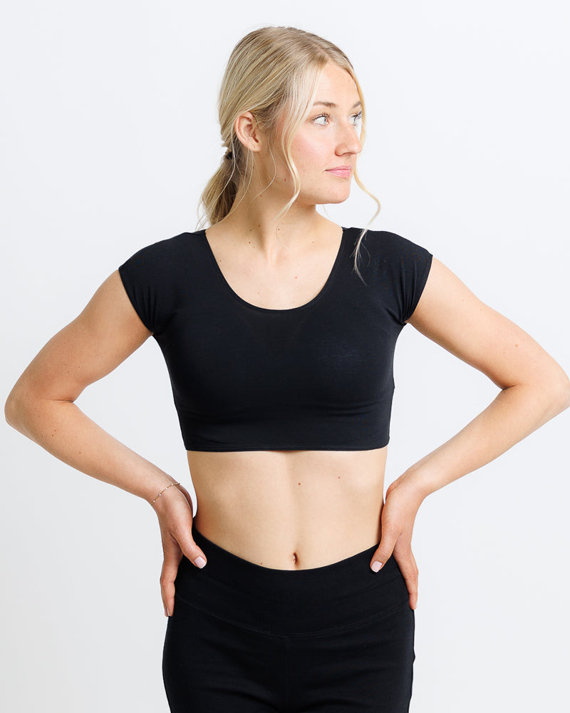 Woman wearing a black crop top and black pants on a white background
