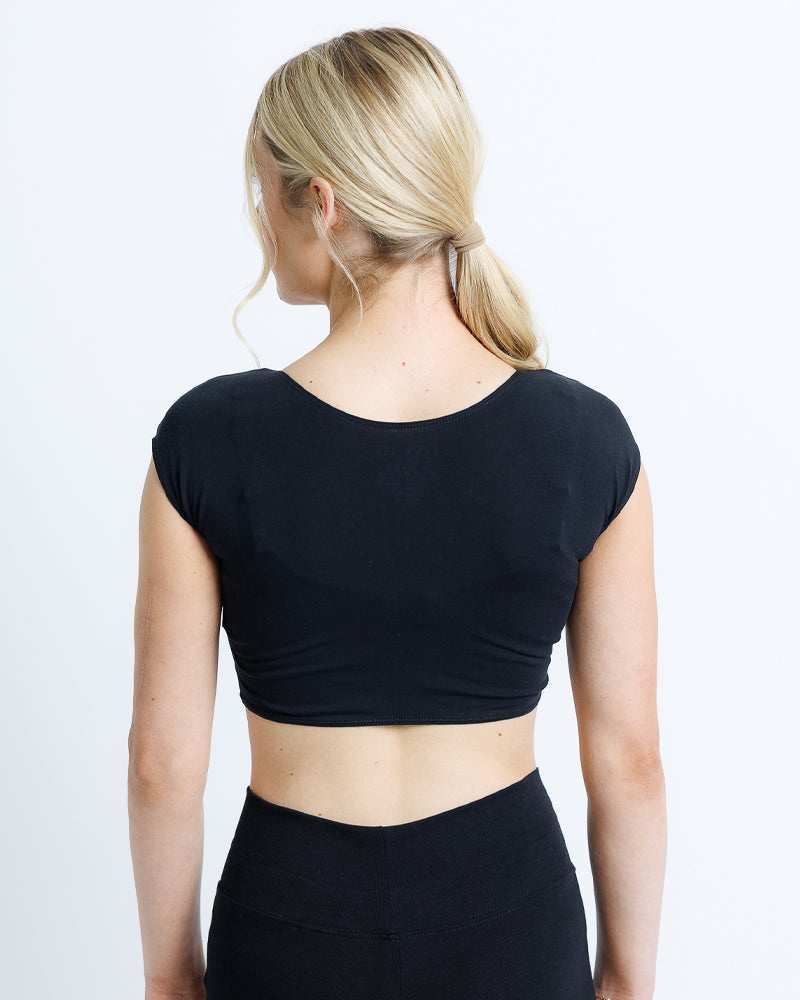 Person wearing a black crop top and black pants on a light gray background