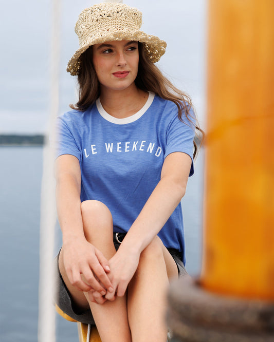 Woman wearing a blue 'Le Week-end' t-shirt and straw hat by a body of water.