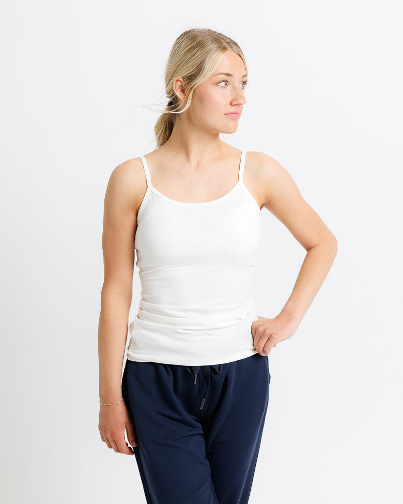 Woman wearing a white tank top and navy pants on a plain background