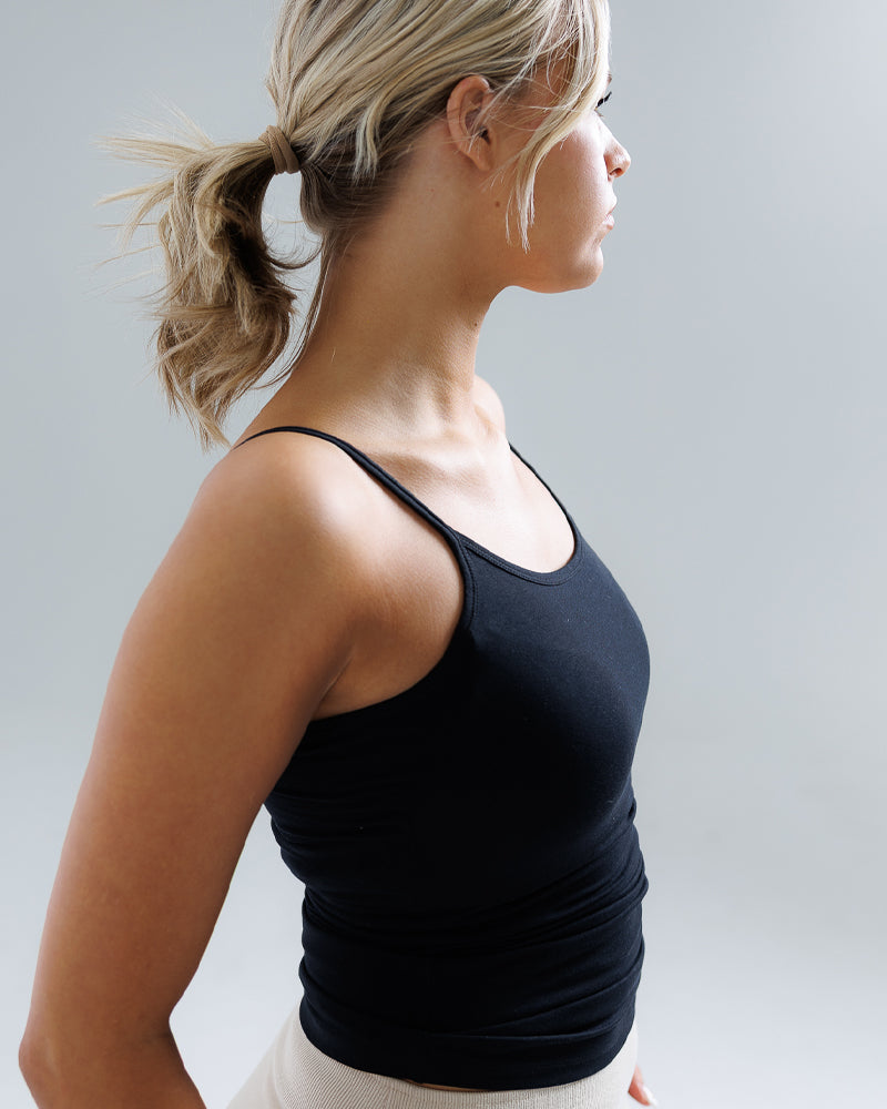 Woman wearing a black tank top against a plain background