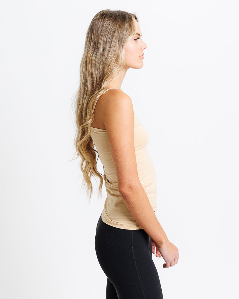 Woman wearing a beige tank top and black leggings on a white background