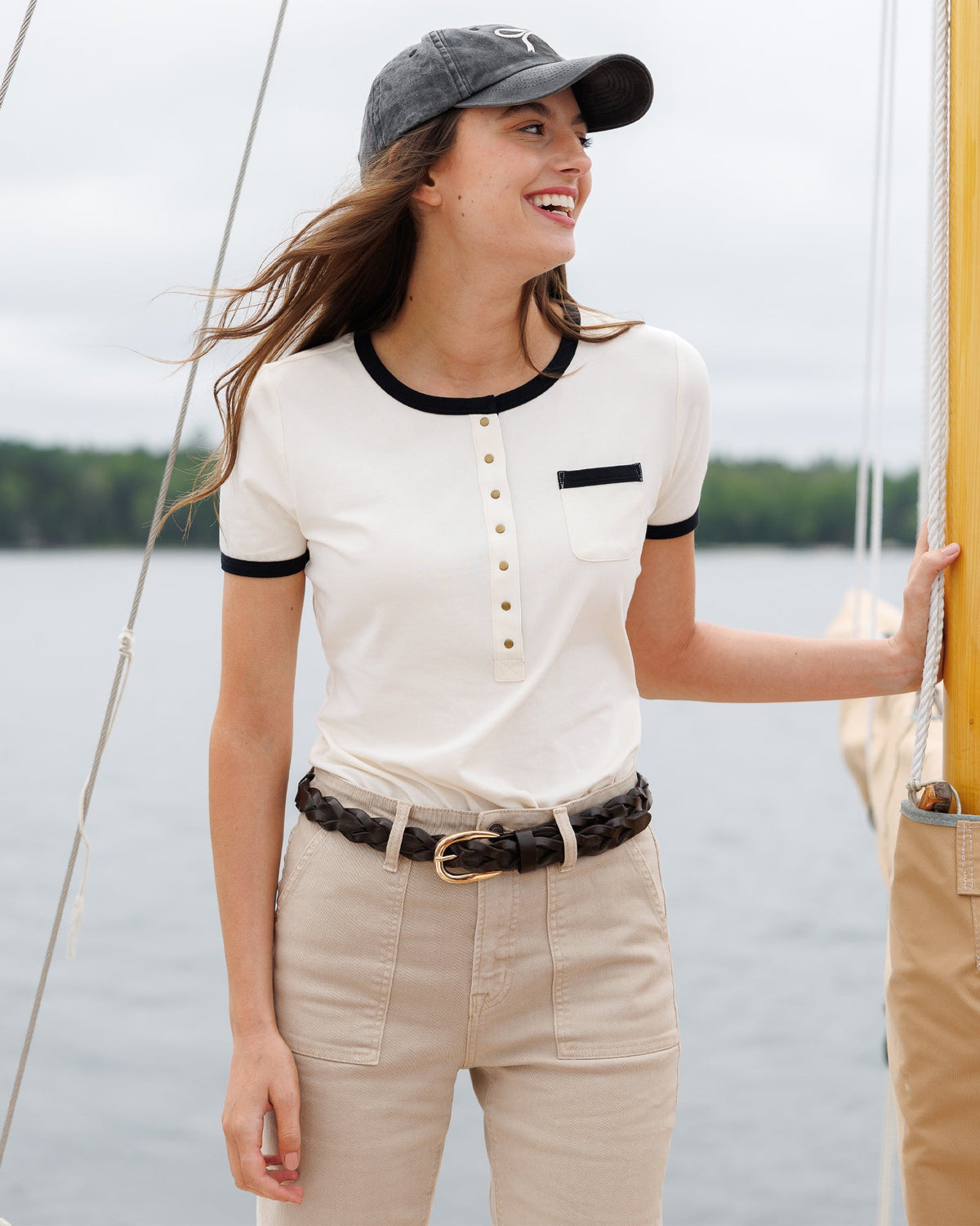 Woman wearing a white shirt with black trim and beige pants by a body of water.