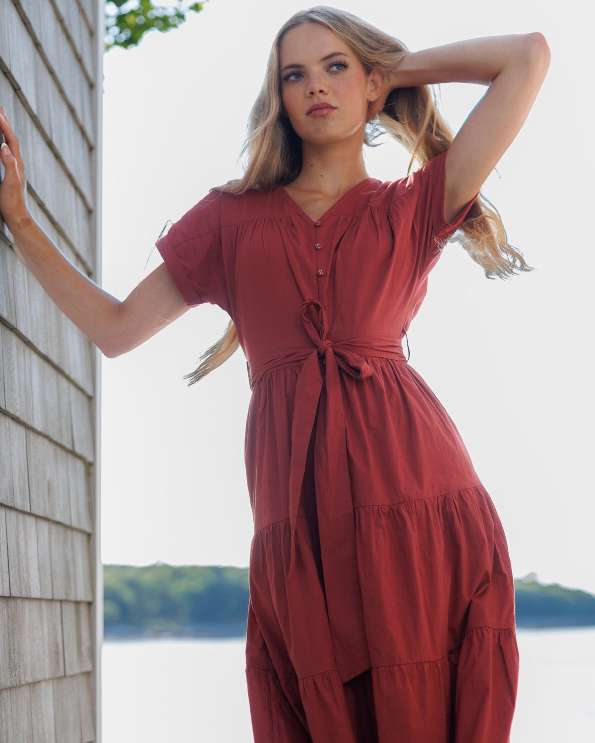 Woman in a red dress standing by a wooden building with a scenic background