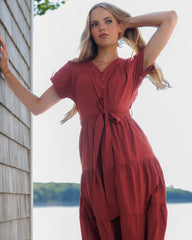 Woman in a red dress standing by a wooden building with a scenic background