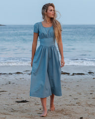 Woman in a blue dress standing on a beach with ocean in the background