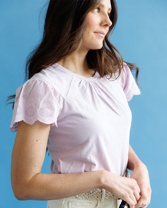 Woman wearing a light pink blouse with ruffled sleeves against a blue background