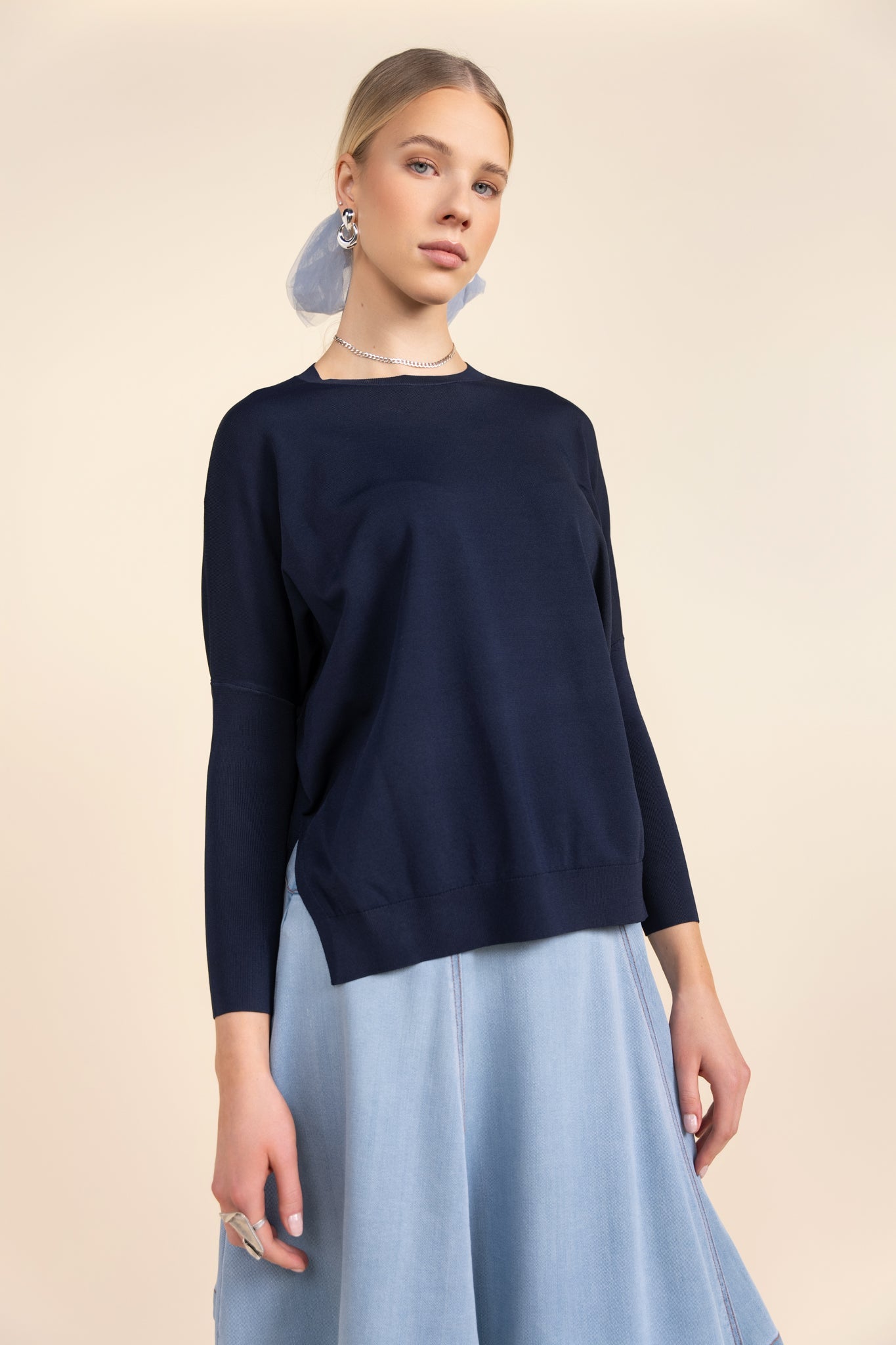 Woman wearing a navy sweater and light blue skirt on a beige background