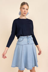 Woman wearing a navy long-sleeve top and light blue denim skirt on a beige background