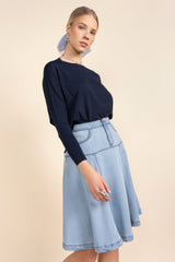 Woman wearing a navy top and light blue skirt on a beige background