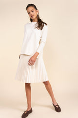 Woman wearing a white sweater and pleated skirt on a beige background